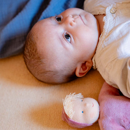 Baby liegt auf einer Decke und schaut nach oben, neben ihm die Käthe Kruse Waldorfpuppe LOLO rose