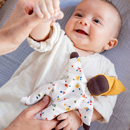Lachendes Baby liegt auf einer Decke, auf seinem Bauch die Käthe Kruse Waldorfpuppe NINI Sonnenschein