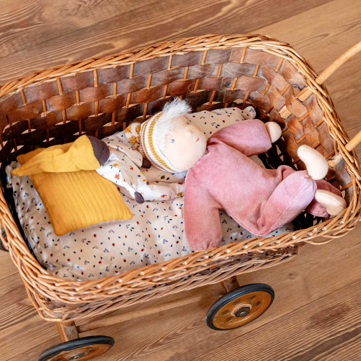 Käthe Kruse Waldorfpuppe NINI Sonnenschein liegt mit zwei anderen Waldorfpuppen in einem Puppenwagen aus Korb