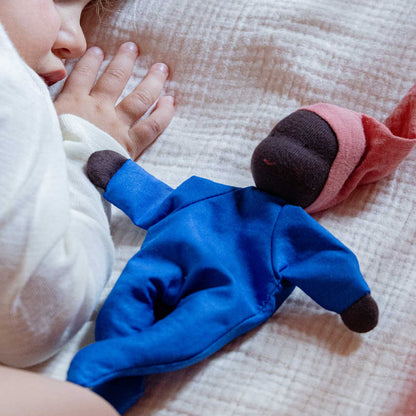 Käthe Kruse Waldorfpuppe NINI Sommerwolke im blauen Anzug liegt auf einer Musselindecke neben einer Kinderhand