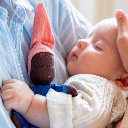 Schlafendes Baby im Arm eines Erwachsenen, an seiner Brust die Käthe Kruse Waldorfpuppe NINI Sommerwolke