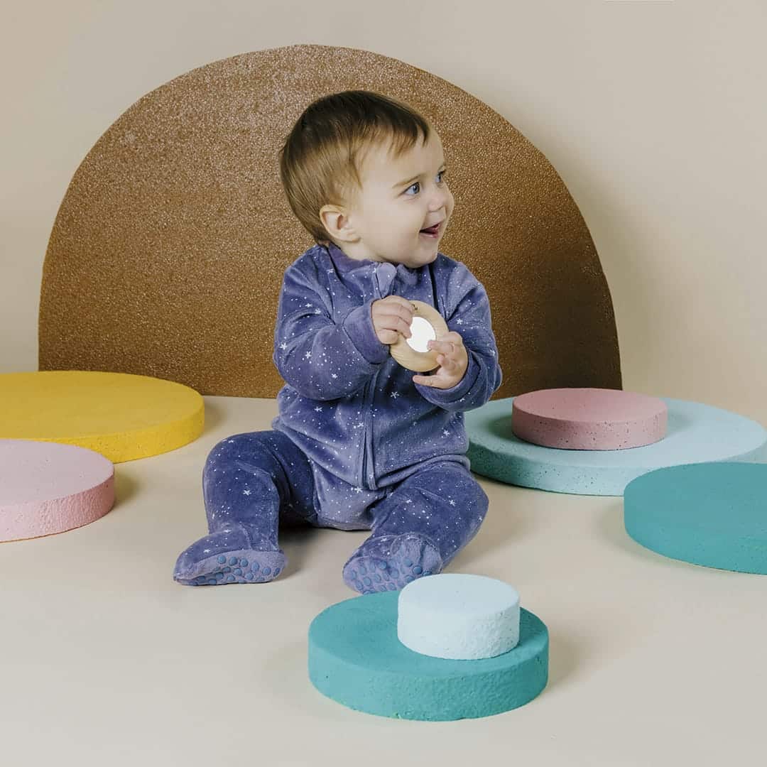 Kleinkind in blauem Strampler sitzt zwischen farbigen runden Podesten und hält einen Reflect Donut
