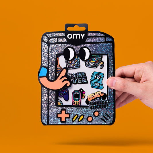 OMY Game Boy Sticker-Packung mit Glitter-Design, bunten Gaming-Motiven, Hand hält Verpackung vor orangem Hintergrund