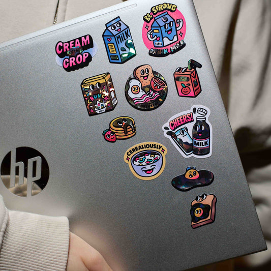 OMY Big Milk Sticker auf silbernem Laptop, bunte Motive wie Milchkarton und Kirsche verteilt