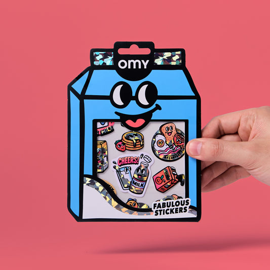 OMY Sticker-Set Big Milk mit bunten Motiven in blauer Milchkarton-Verpackung, Hand hält das Paket von rechts