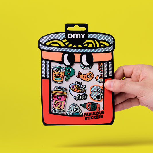 OMY Big Noodle Sticker, rote Behältnis-Packung mit Fenster voller bunter Sticker-Motive, Hand hält die Verpackung