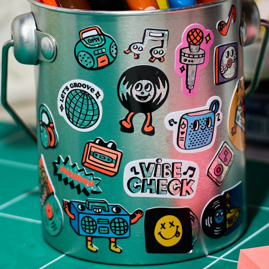 Metallbecher mit bunten Musik-Stickern von OMY Iconic, darunter Roboter, Kopfhörer, Kassette, Smiley und Text Vibe Check