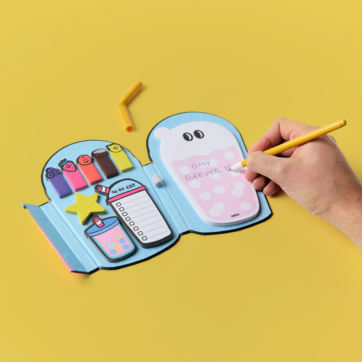 Hand schreibt mit Holzstift auf die Notizseite der geöffneten OMY Bubble Notes Haftnotizen in Blau