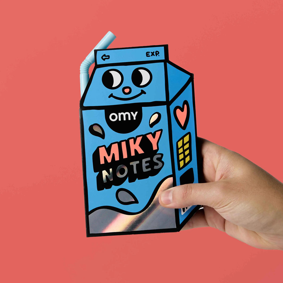 OMY Miky Notes Haftnotizen in blauer Milchkarton-Form mit lachendem Gesicht, in einer Hand gehalten vor rosa Hintergrund