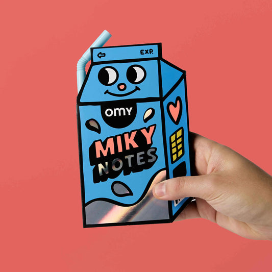 OMY Miky Notes Haftnotizen in blauer Milchkarton-Form mit lachendem Gesicht, in einer Hand gehalten vor rosa Hintergrund