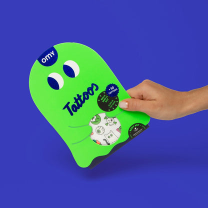 OMY Tattoos Boo, grüne Gespenster-Verpackung mit weißen Augen, Hand hält sie vor blauem Hintergrund