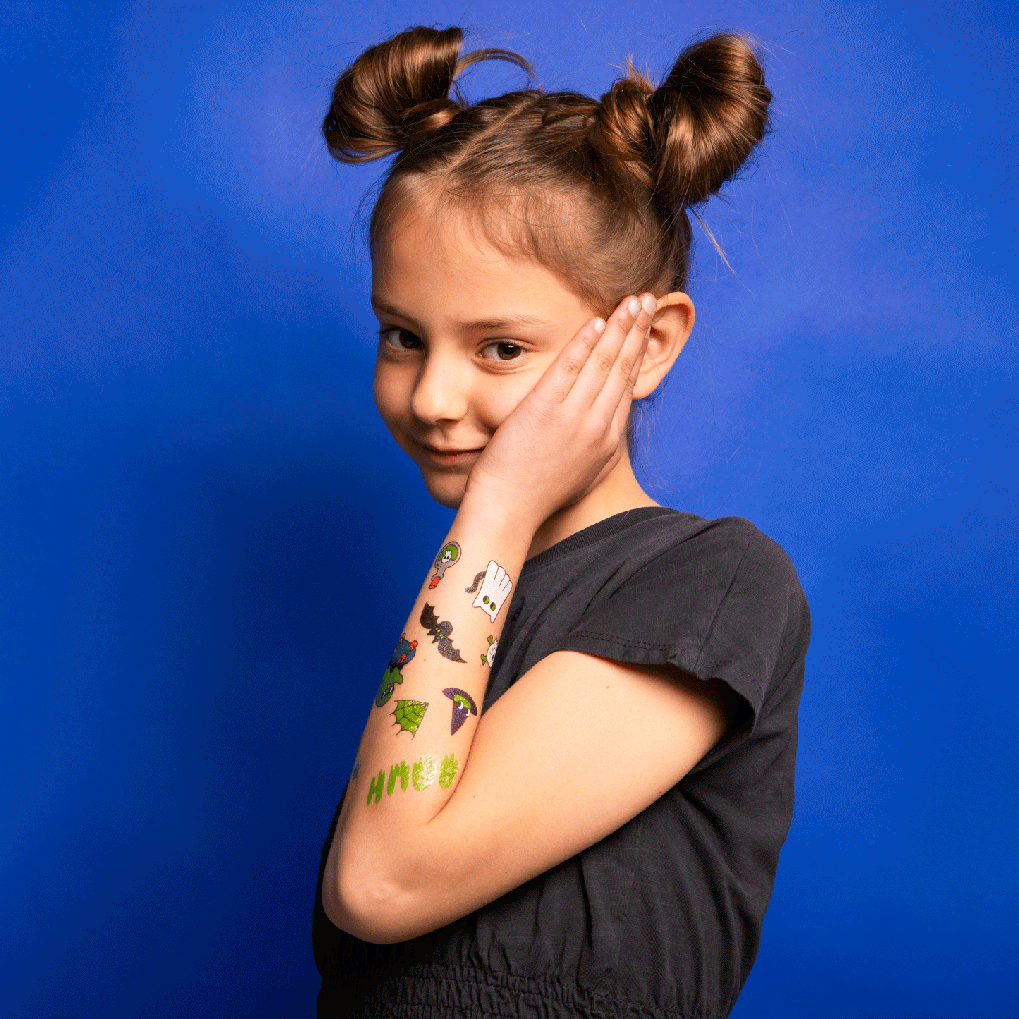 Mädchen mit OMY Tattoos Boo auf Arm und Wange, bunte Halloween-Motive, schwarzes Shirt