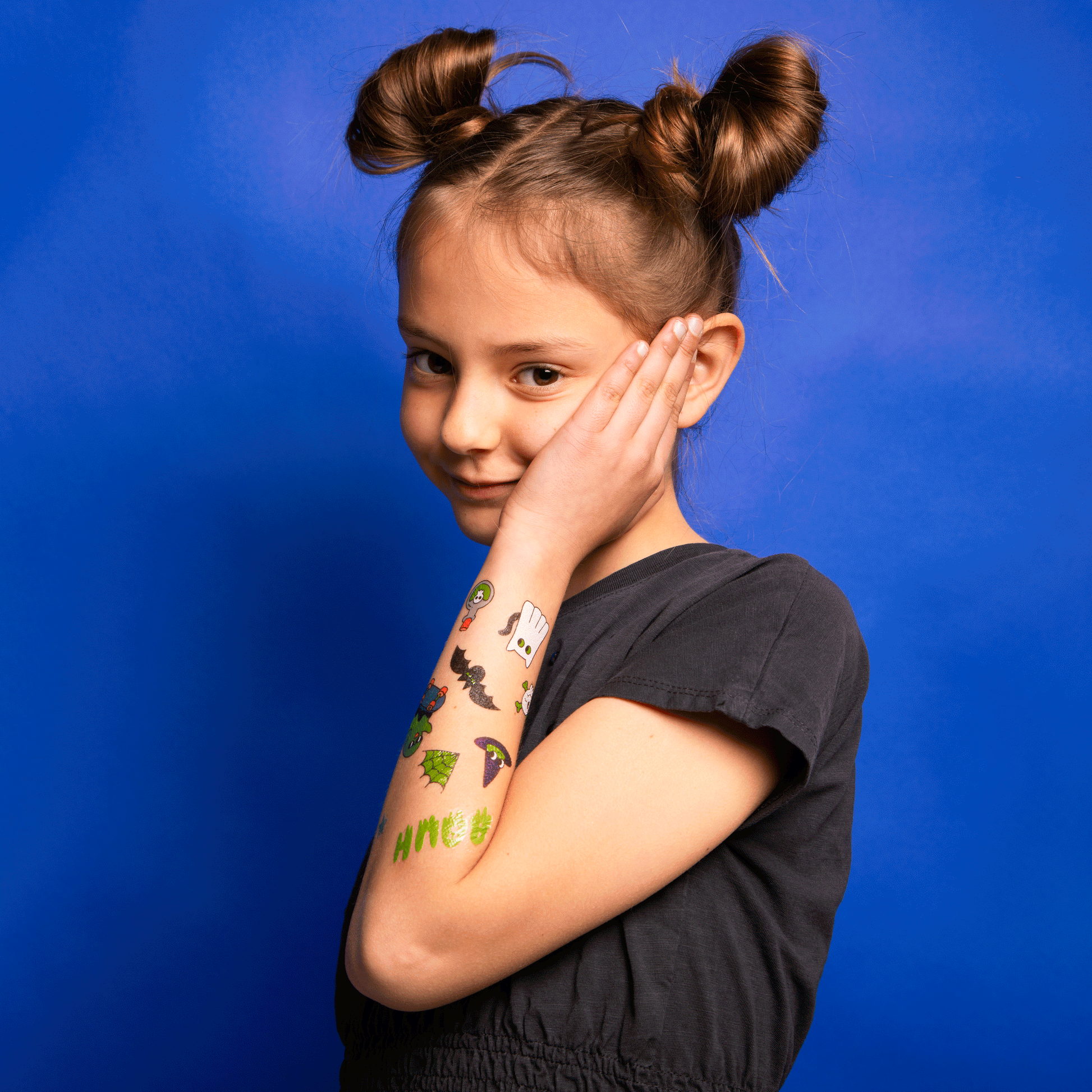 Mädchen mit OMY Tattoos Boo auf Arm und Wange, bunte Halloween-Motive, schwarzes Shirt