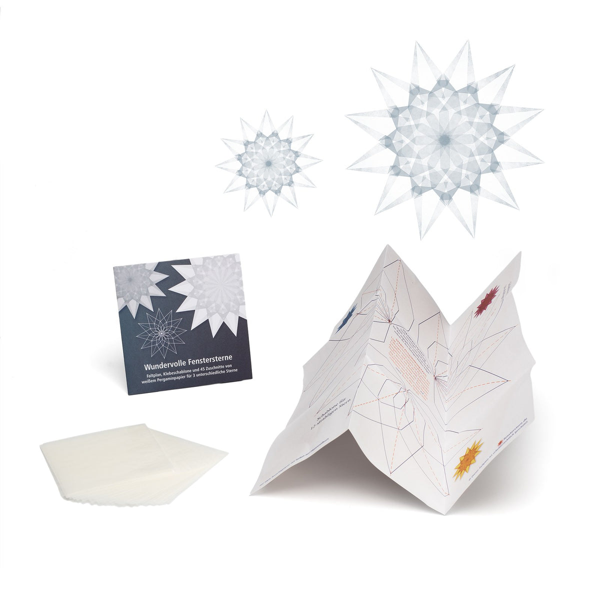 Ausgepacktes Set Wundervolle Fenstersterne in Weiß: Kartontasche, weißes Pergaminpapier, aufgestellter Faltplan und zwei fertige weiße Sterne
