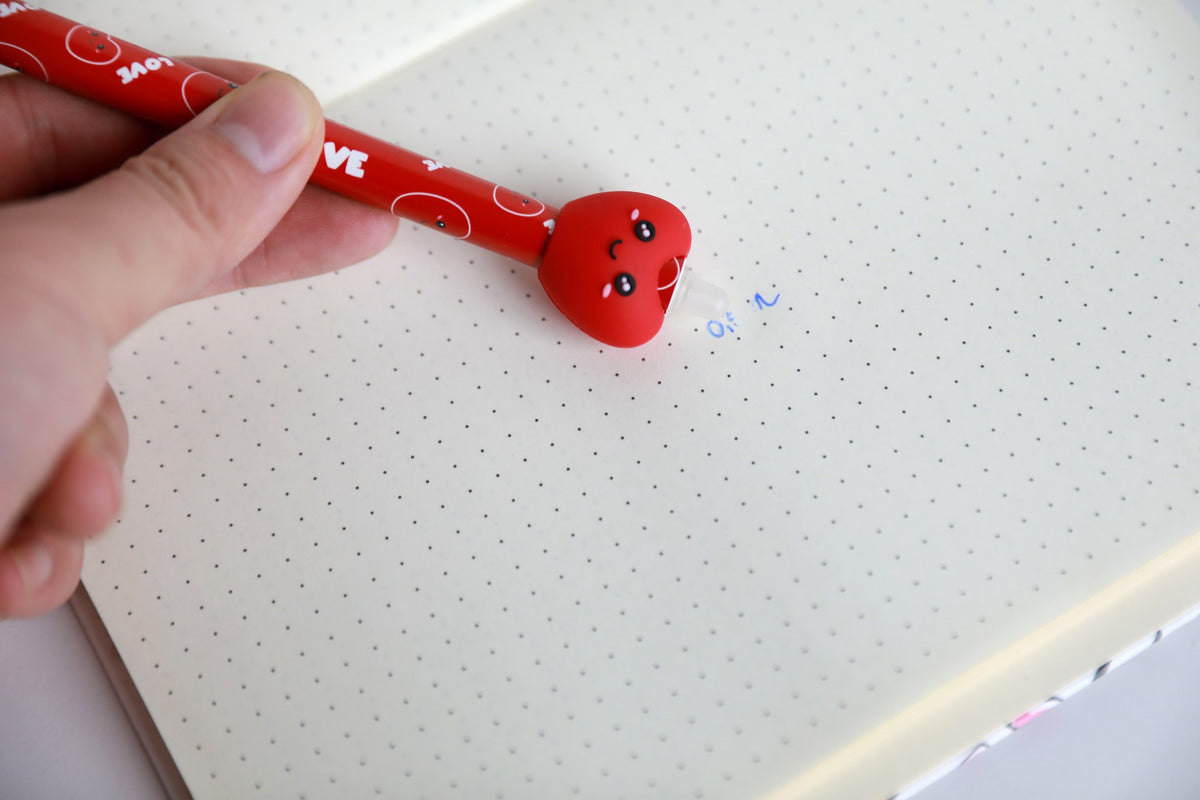Hand hält den Stift mit Figur Herz und radiert damit Schrift auf Punktrasterpapier