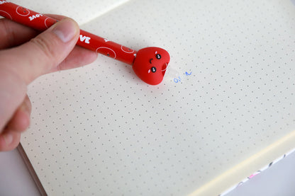 Hand hält den Stift mit Figur Herz und radiert damit Schrift auf Punktrasterpapier