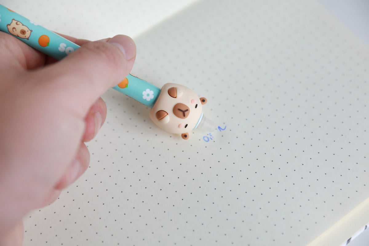 Hand hält den Stift mit Figur Capybara und radiert damit Schrift auf Punktrasterpapier