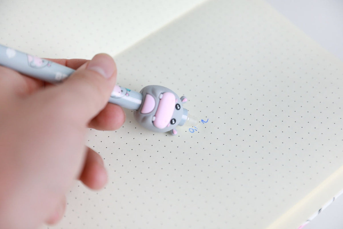Hand hält den Stift mit Figur Nilpferd und radiert damit Schrift auf Punktrasterpapier