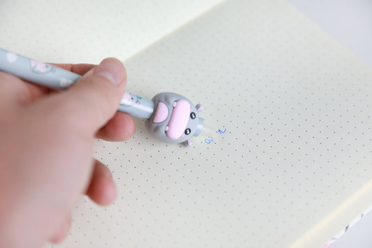 Hand hält den Stift mit Figur Nilpferd und radiert damit Schrift auf Punktrasterpapier