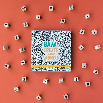 Londji BAM! Stempelset mit Verpackung, umgeben von Buchstabenwürfeln auf orangefarbenem Hintergrund