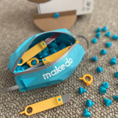 Makedo Tool-Case Tasche geöffnet mit gelben Werkzeugen, blauen Scrus und Kunststoffteilen auf grauem Teppich verteilt