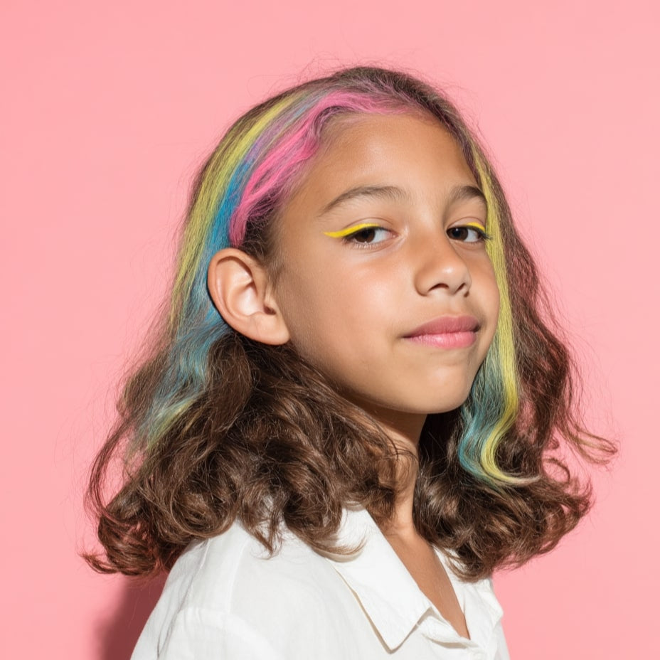 Kind mit weißer Bluse vor rosa Hintergrund, Haare mit OMY Haarkreide in Gelb, Rosa, Blau und Grün gefärbt