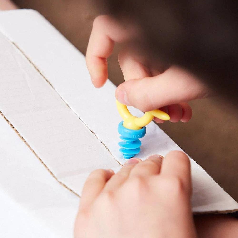 Kind baut mit Makedo Verbindern und Karton, ein türkiser und gelber Konstruktionsteil werden zusammengefügt