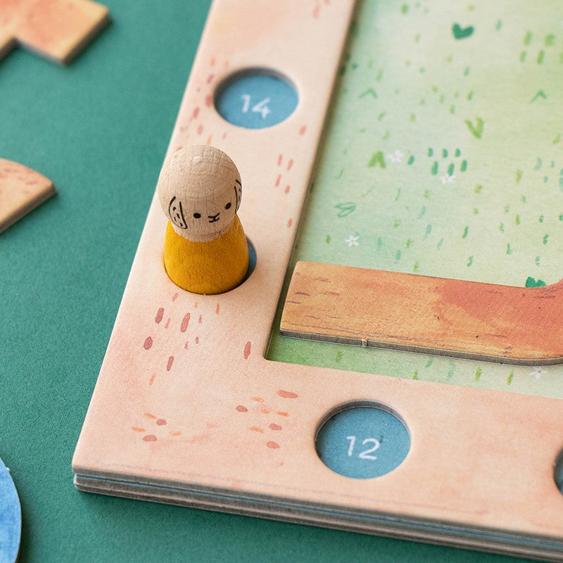 Londji Best Friends Spiel, Detailaufnahme einer Holzfigur mit gelbem Kleid und Knopf mit Nummer 14 auf pastellrosa Brett