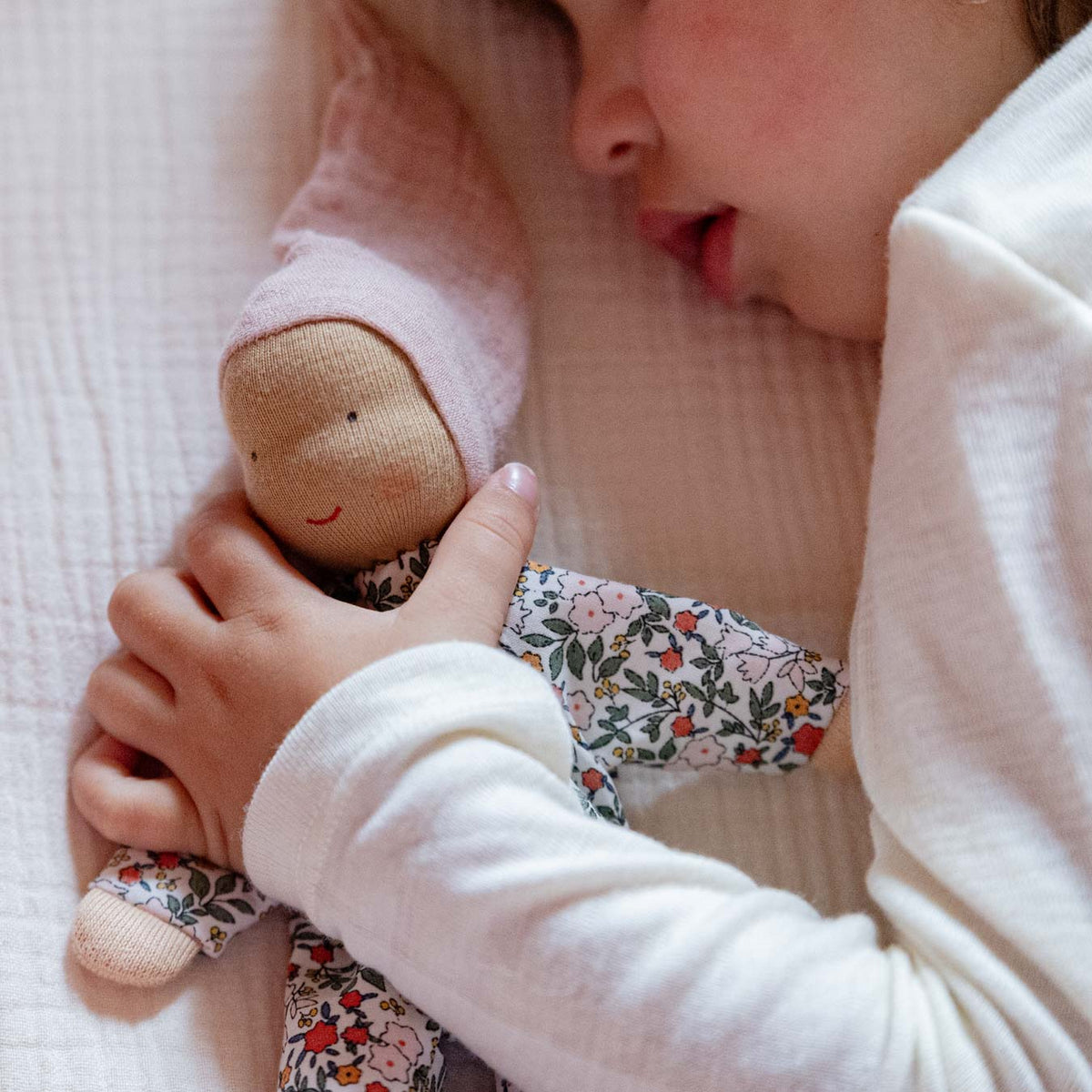 Schlafendes Kind hält die Käthe Kruse Waldorfpuppe NINI Blümchen mit rosa Zipfelmütze an sich gedrückt