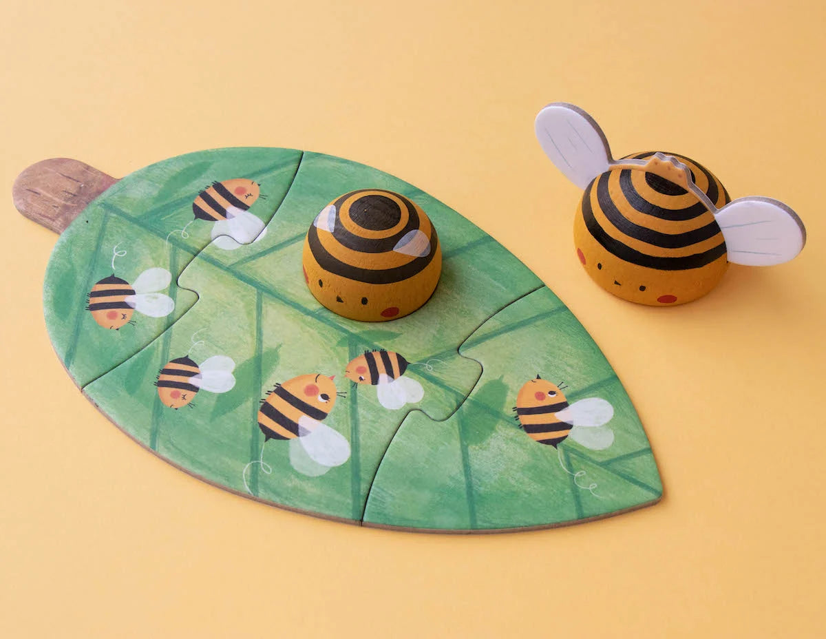 Londji Bzzz: grünes Blatt-Puzzle mit gemalten Bienen, daneben zwei Holzbienen