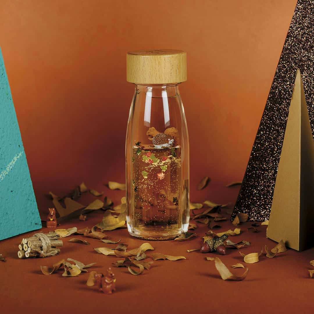 Petit Boum Move Bottle Autumn Sensorikflasche mit Holzverschluss auf herbstlichem Untergrund mit getrockneten Blättern