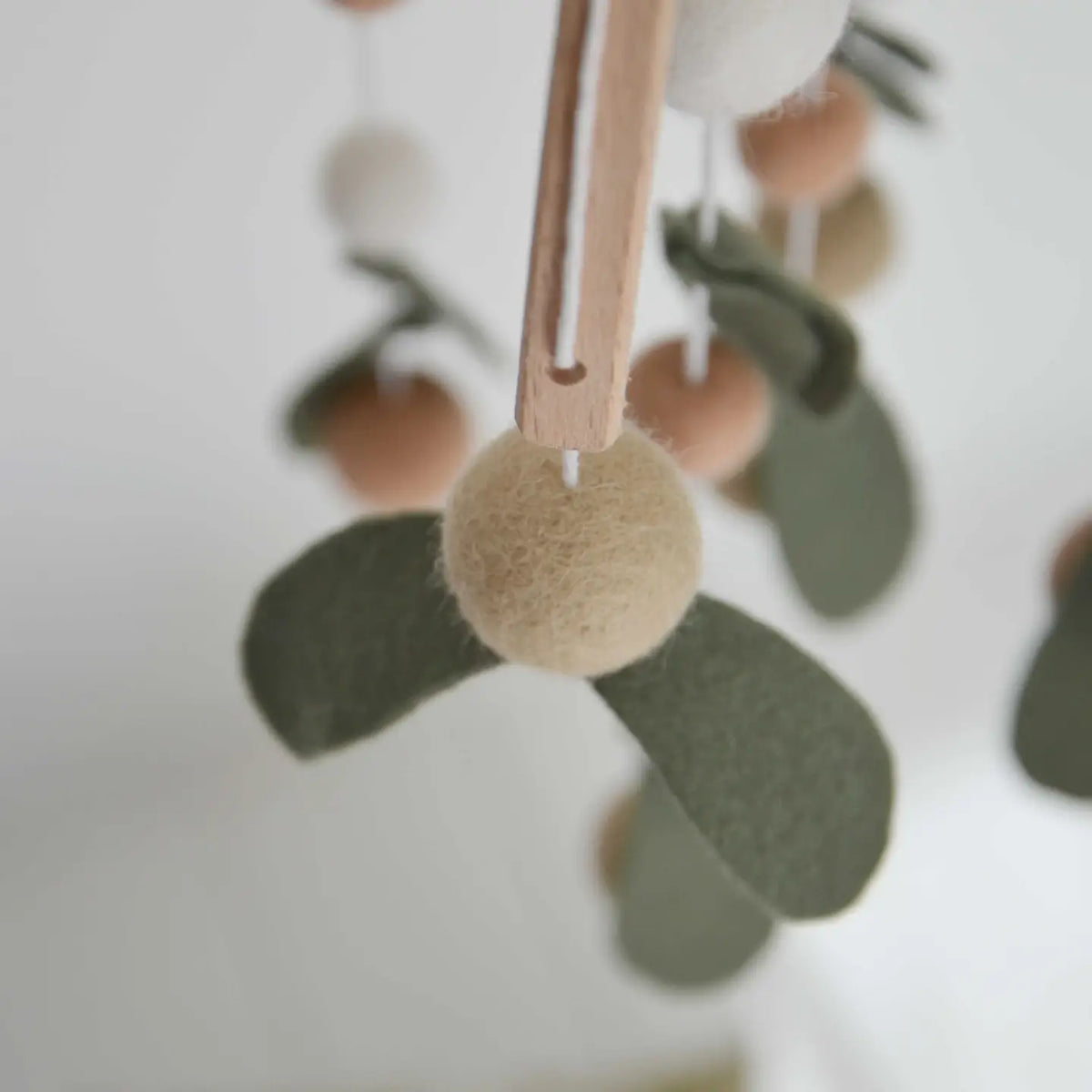 Nahaufnahme: beige Filzkugel mit zwei grünen Filzblättern am Holzbogen des CALM Mobiles