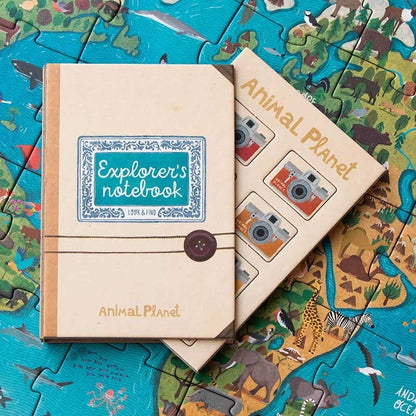 Londji Animal Planet Notizbuch mit beigem Leinen neben Notizbuch mit Tierfoto-Puzzleteilen auf ausgebreitetem Puzzle
