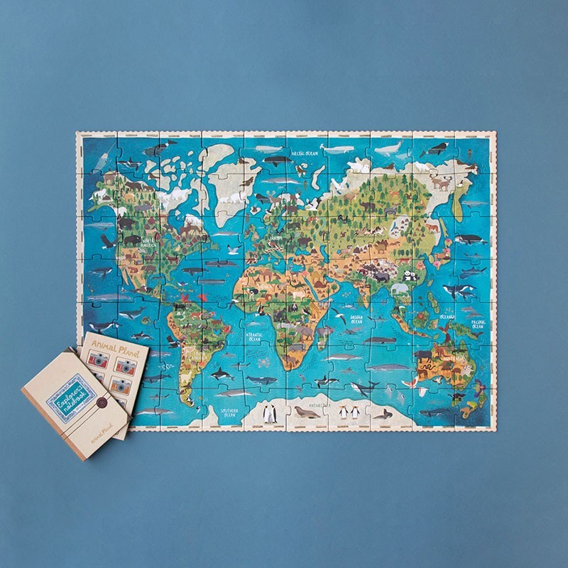 Londji Animal Planet Puzzle mit Weltkarte und bunten Tierillustrationen, beiges Notizbuch daneben auf blauem Grund