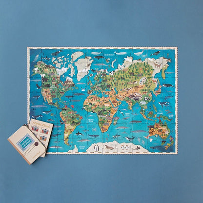 Londji Animal Planet Puzzle mit Weltkarte und bunten Tierillustrationen, beiges Notizbuch daneben auf blauem Grund