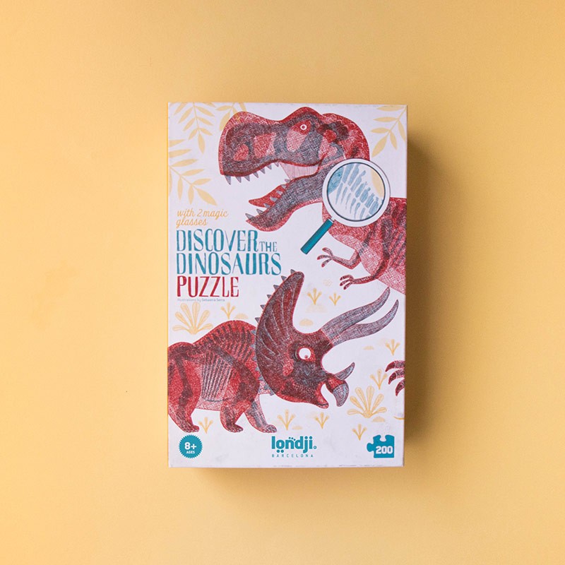 Verpackung des Londji Discover Dinosaurs Puzzles mit roten Dinosauriern und Lupe auf cremefarbenem Hintergrund