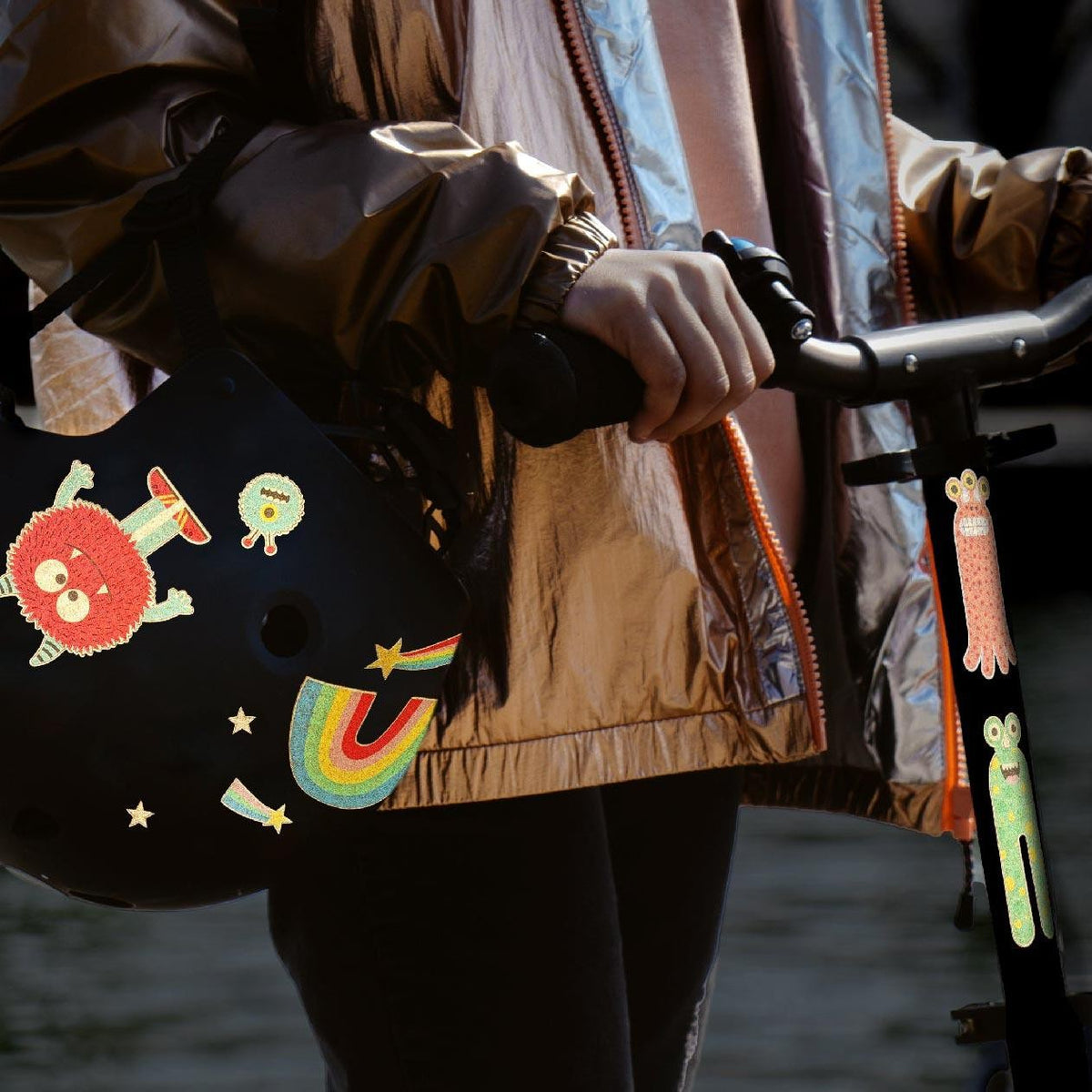 Person hält einen schwarzen Fahrradhelm mit reflektierenden Rainette Stickern, darunter ein Regenbogen